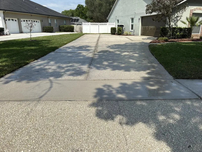 Clean bright long driveway leading to a white vinyl gate after pressure washing