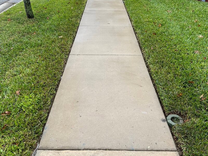 Spotless white vinyl fence running along a green backyard lawn after cleaning